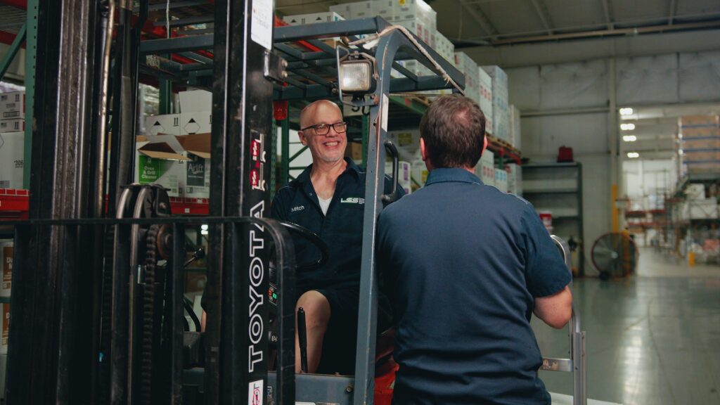 An LSS warehouse team member on a forklift talking with a coworker